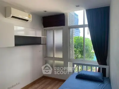 Cozy bedroom with large window and air conditioning, offering a serene view of greenery.