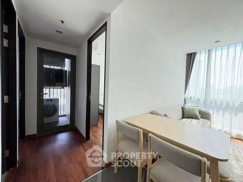 Modern apartment interior with dining area and balcony view, featuring sleek furniture and natural light.
