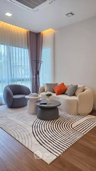 Modern living room with stylish furniture and large windows, featuring a cozy sofa and armchair on a patterned rug.