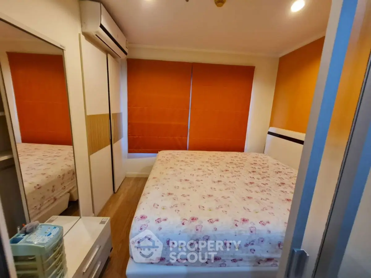 Cozy bedroom with floral bedding and orange blinds, featuring mirrored wardrobe and air conditioning.