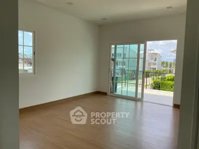 Spacious empty room with wooden flooring and large sliding glass doors leading to a balcony with a view.