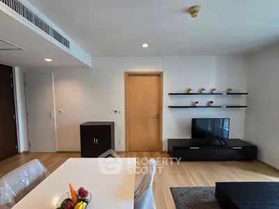 Modern living room with sleek furniture and wooden flooring, featuring a TV and decorative shelves.