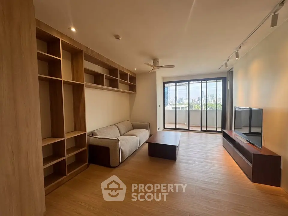 Spacious modern living room with built-in shelves and city view balcony.