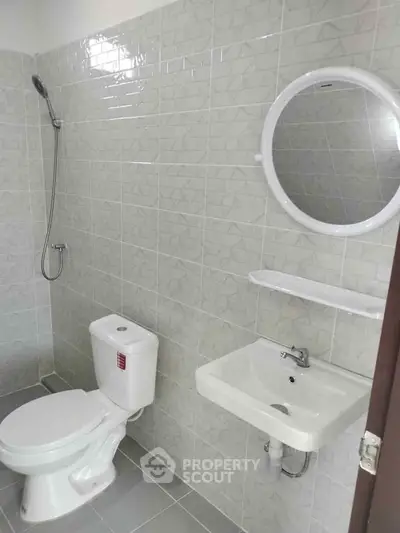 Modern bathroom with sleek fixtures and tiled walls, featuring a round mirror and compact design.