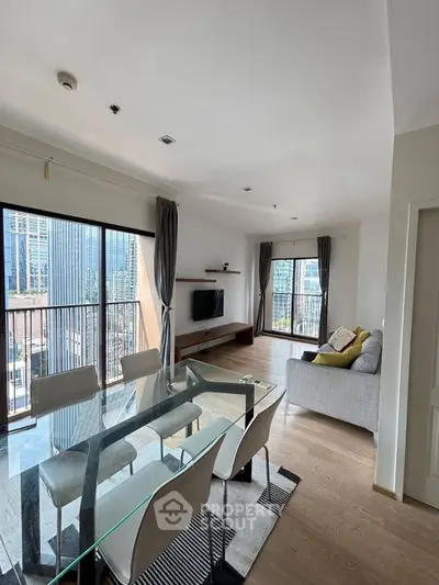 Modern living room with glass dining table and city view from large windows.