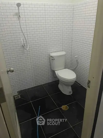 Modern bathroom with sleek black tiles and white subway tile walls, featuring a toilet and shower.