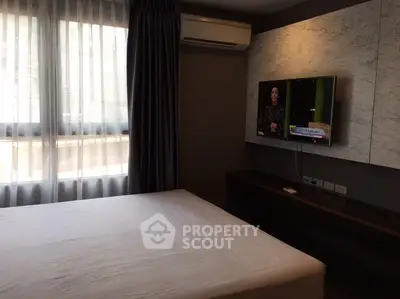 Cozy bedroom with air conditioning and wall-mounted TV, featuring large window with sheer curtains.