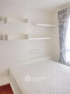 Minimalist bedroom with white shelves and mattress, featuring natural light from window.