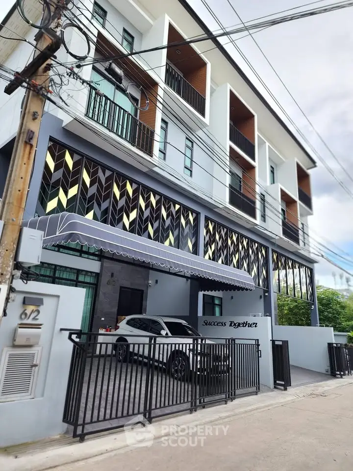 Modern multi-story building with stylish facade and gated parking area.