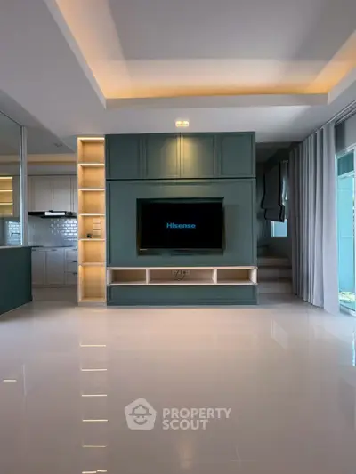 Modern living room with built-in TV unit and open kitchen layout, featuring sleek design and ambient lighting.