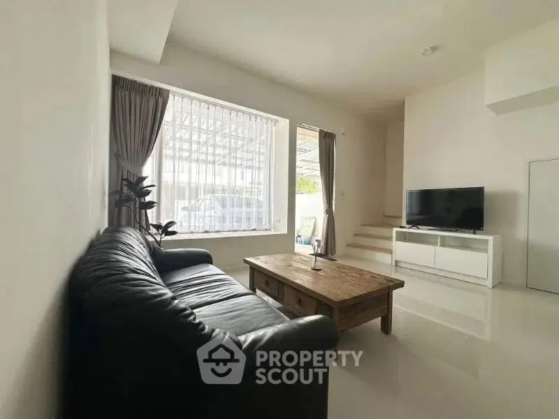Spacious living room with sleek black sofa and modern TV setup, ideal for relaxation.