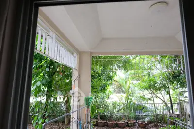 Charming garden view from a covered balcony with lush greenery and potted plants.
