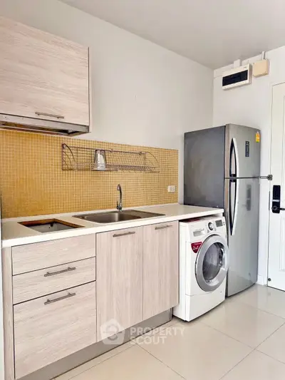 Modern kitchen with sleek cabinets, washing machine, and stainless steel fridge.