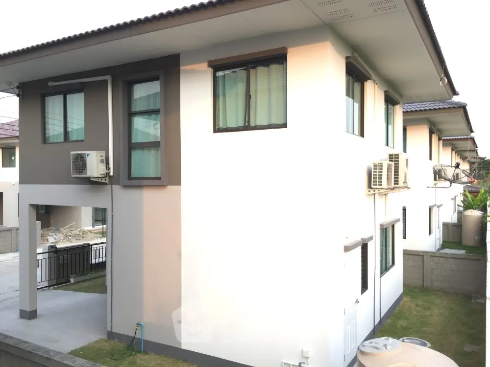 Modern two-story house with air conditioning units and a small garden area.