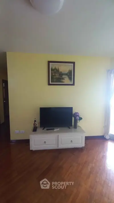 Cozy living room with TV and wooden flooring, perfect for relaxation.