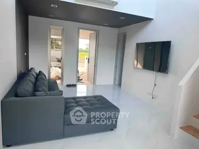 Modern living room with sleek gray sofa and wall-mounted TV, featuring minimalist design and natural light.