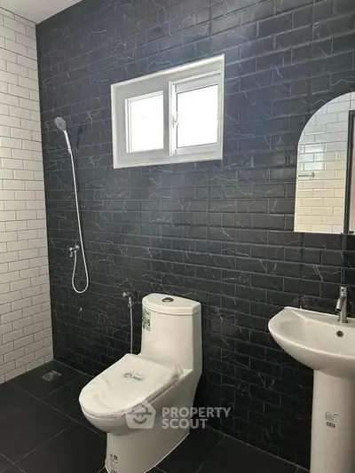 Modern bathroom with sleek black and white tiles, featuring a toilet, sink, and shower area.