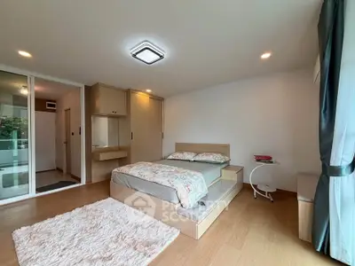 Spacious modern bedroom with wooden flooring and large window for natural light.