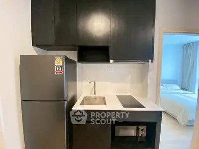Modern compact kitchen with sleek black cabinets and stainless steel appliances in a cozy apartment.