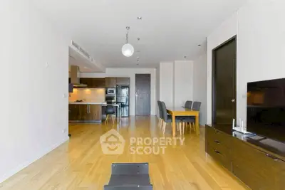 Spacious modern living room with open kitchen and dining area, featuring sleek wooden flooring.