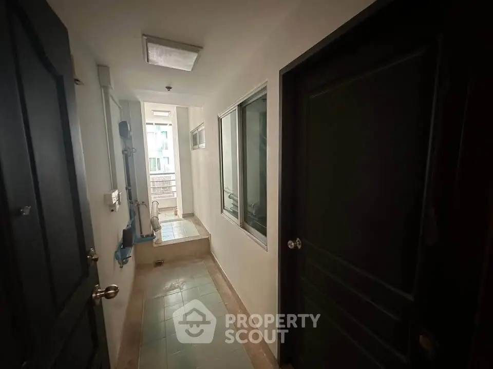 Narrow corridor with doors and windows in a residential building, showcasing a compact layout.