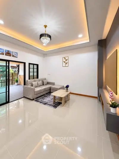 Spacious modern living room with elegant chandelier and large sliding doors opening to a garden view.