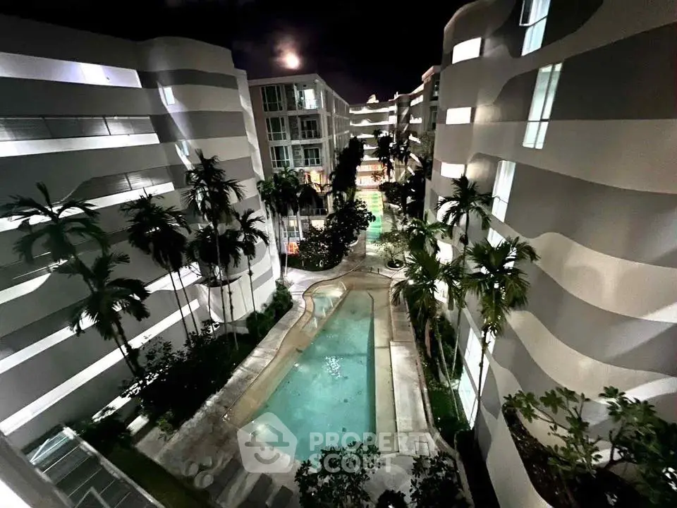 Stunning night view of modern apartment complex with illuminated pool and palm trees.