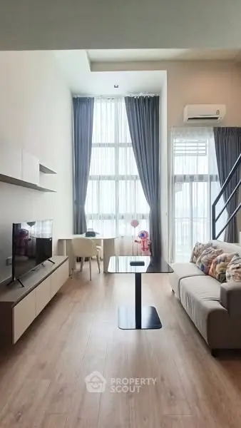 Modern living room with high ceilings and large windows, featuring stylish furniture and a cozy atmosphere.