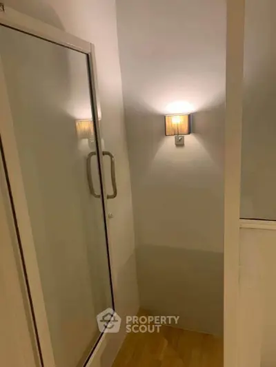 Modern bathroom corner with glass shower door and wall sconce lighting.