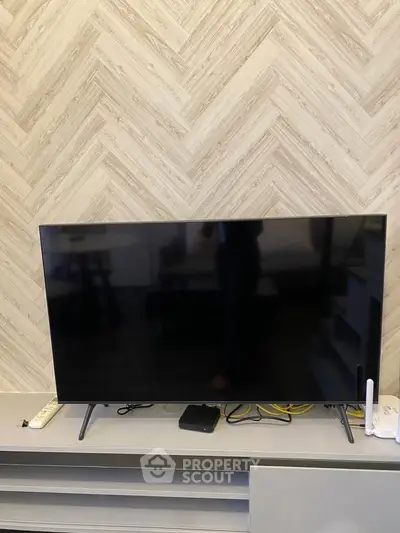 Modern living room with sleek TV setup and stylish herringbone wall design.