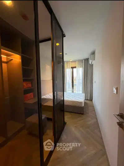 Modern bedroom with glass partition and stylish herringbone flooring, featuring a cozy bed and ample natural light.