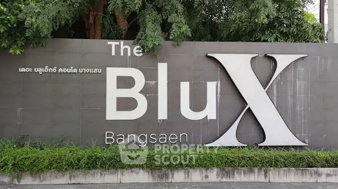 The Blu X Bangsaen modern residential building entrance sign with lush greenery.