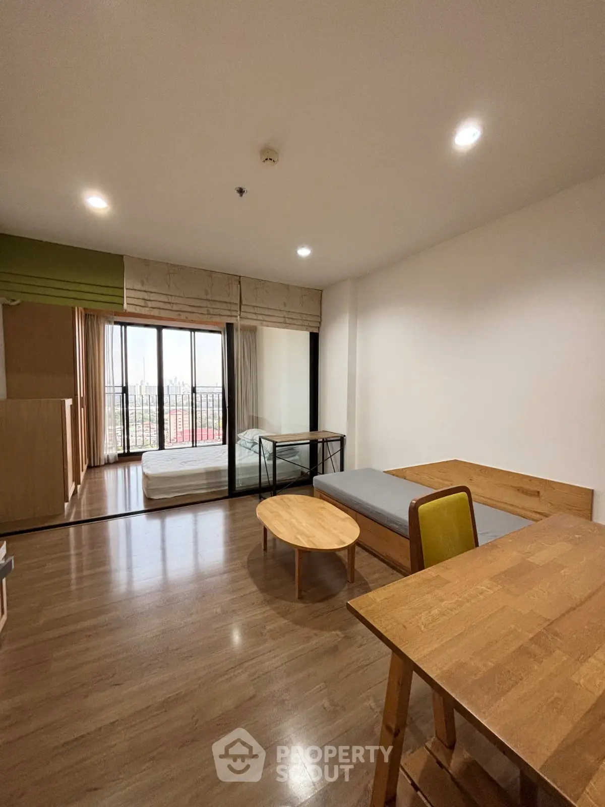 Spacious studio apartment with wooden flooring and large windows offering city views.