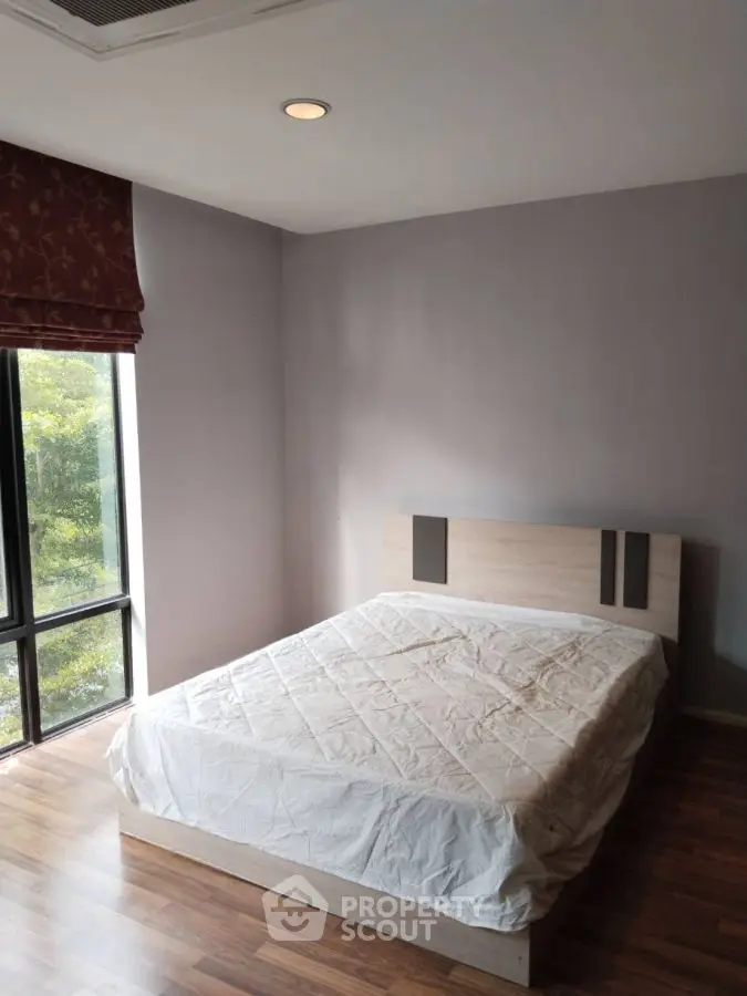 Cozy bedroom with large window and modern bed frame, offering serene natural views.