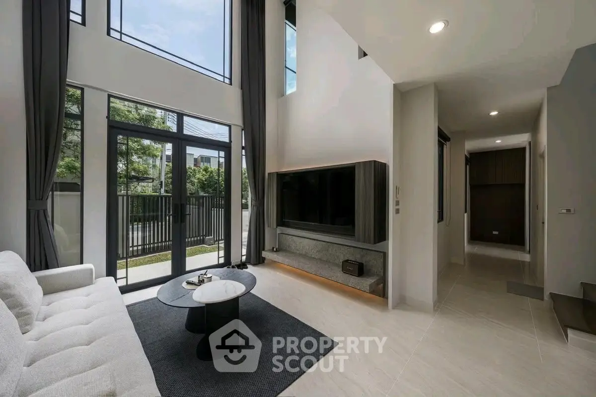 Spacious modern living room with high ceilings and large windows offering natural light and garden view.
