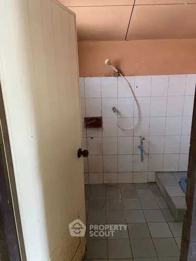 Basic bathroom with showerhead and tiled walls, ideal for renovation.