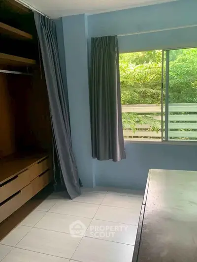 Spacious bedroom with large window and built-in closet overlooking lush greenery.