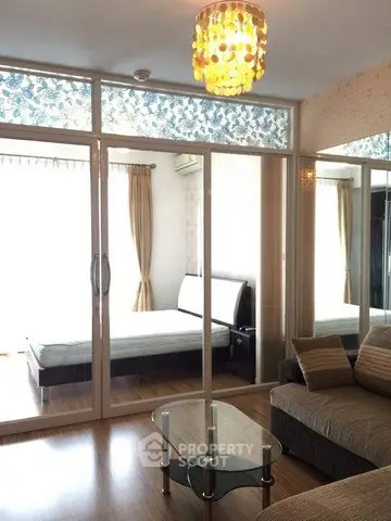 Modern living room with glass partition leading to a stylish bedroom, featuring elegant decor and natural light.
