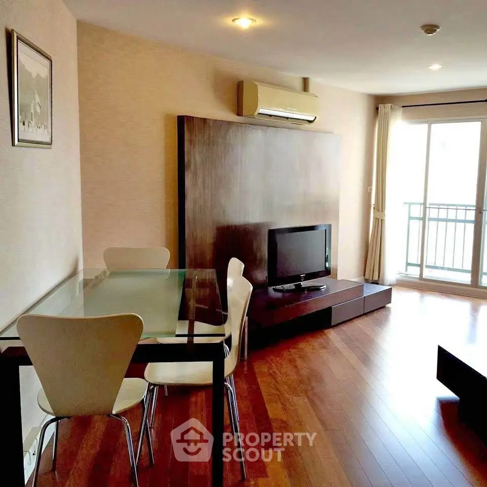 Modern living room with wooden flooring, glass dining table, and balcony access.