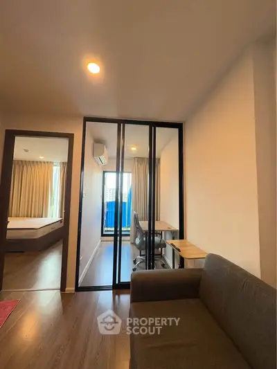 Modern apartment interior with cozy living room and study area, featuring glass partition and natural light.