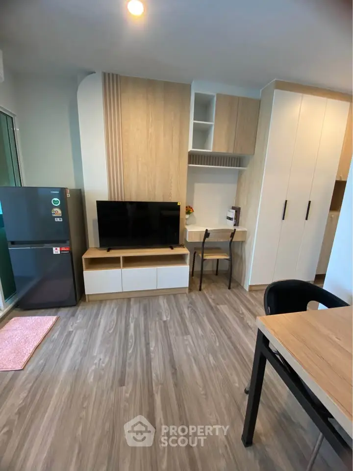 Modern living room with sleek furniture and wooden flooring, featuring a TV and compact workspace.