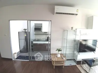 Modern living room with sleek kitchen and glass cabinets, featuring air conditioning and stylish decor.