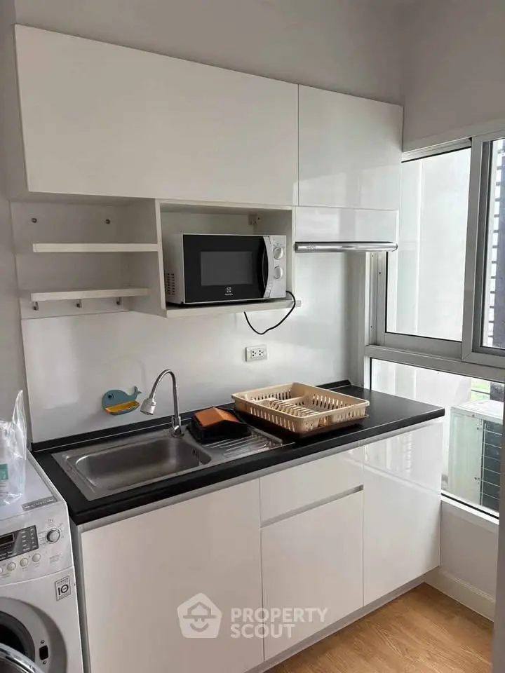 Modern kitchen with sleek white cabinets, microwave, and washing machine in a compact layout.