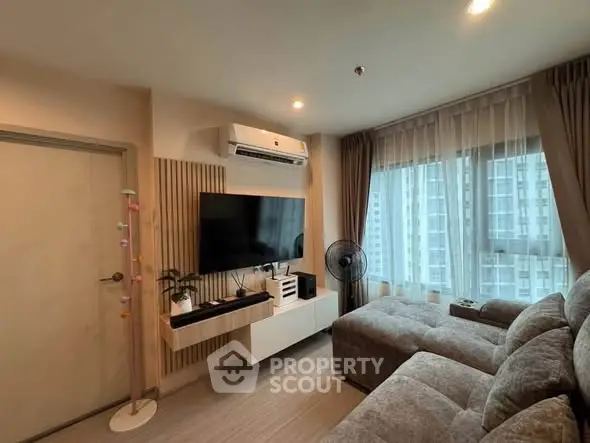 Modern living room with cozy sofa, wall-mounted TV, and large window with city view.
