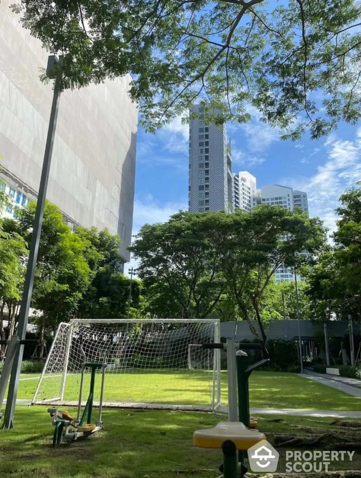 Urban garden with exercise equipment and soccer goal, surrounded by modern high-rise buildings.