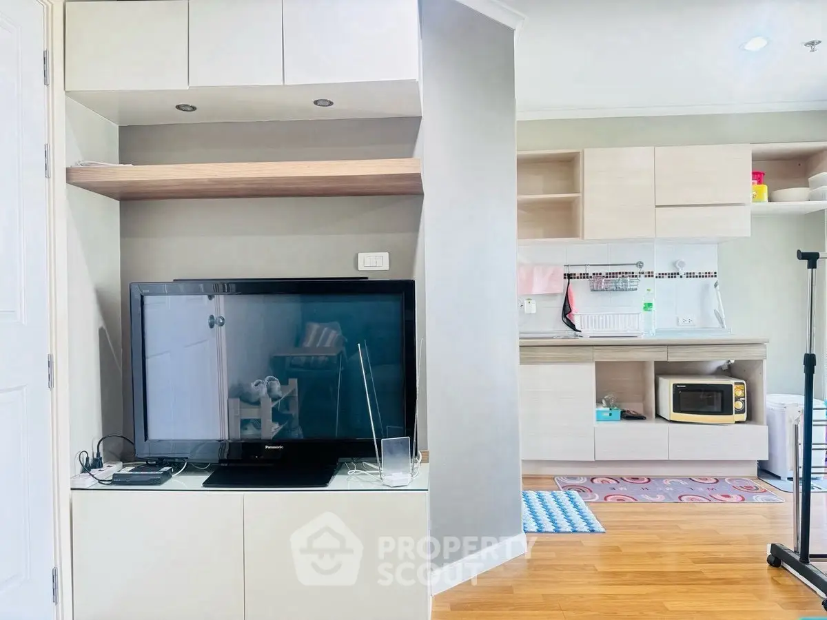 Modern living room with TV and open kitchen layout, featuring sleek cabinetry and hardwood floors.