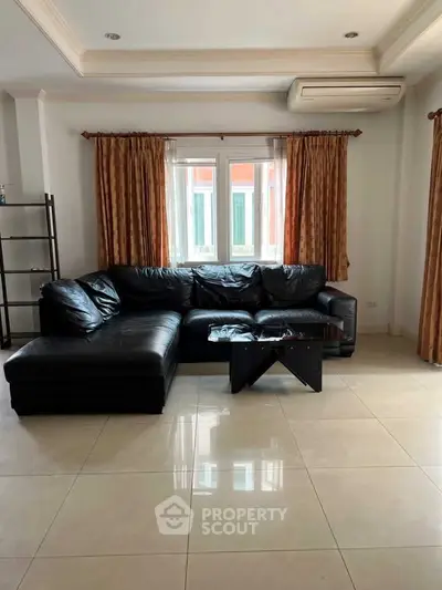 Spacious living room with black leather sectional sofa and large window, perfect for relaxation.