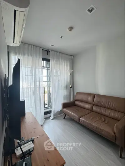 Cozy living room with leather sofa, TV, and large window with sheer curtains in modern apartment.