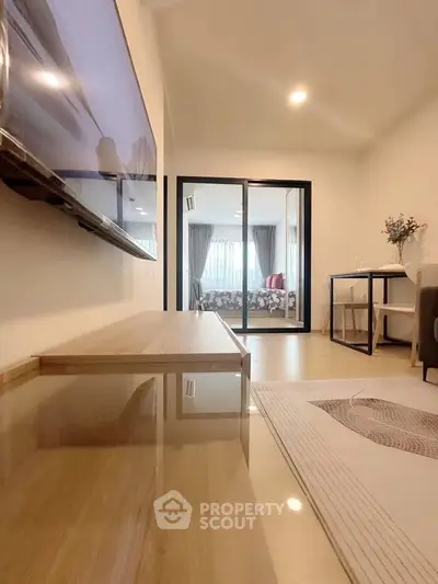 Modern living room with sleek furniture and large TV, leading to a bright bedroom with glass doors.