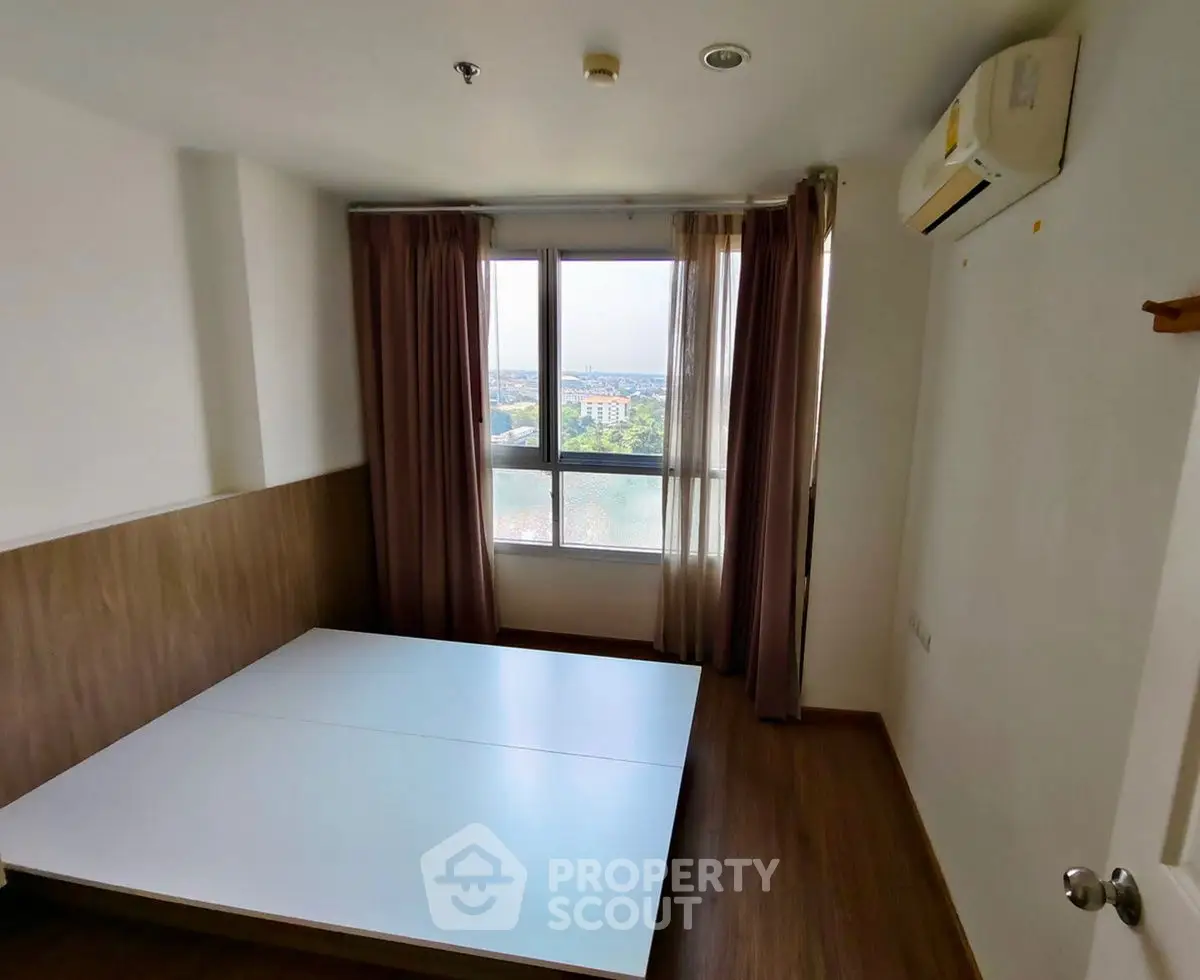 Spacious bedroom with large window offering a scenic view, featuring wooden flooring and modern air conditioning.